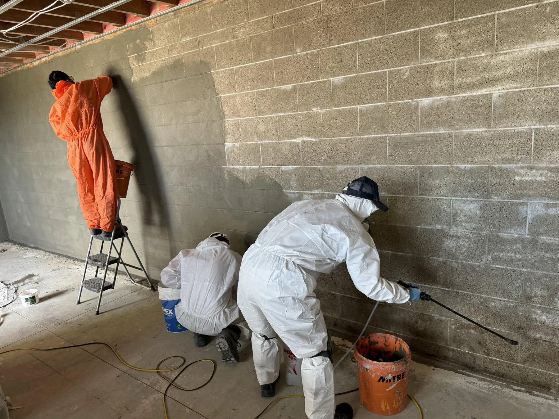Applicators treating a concrete block wall with crystalline waterproofing material