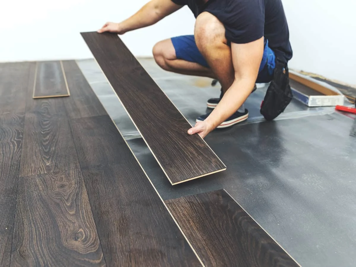 Flooring installer fitting dark wood-look laminate planks over prepared underlay