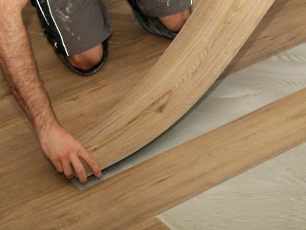 Flooring installer laying flexible wood-look residential vinyl over adhesive